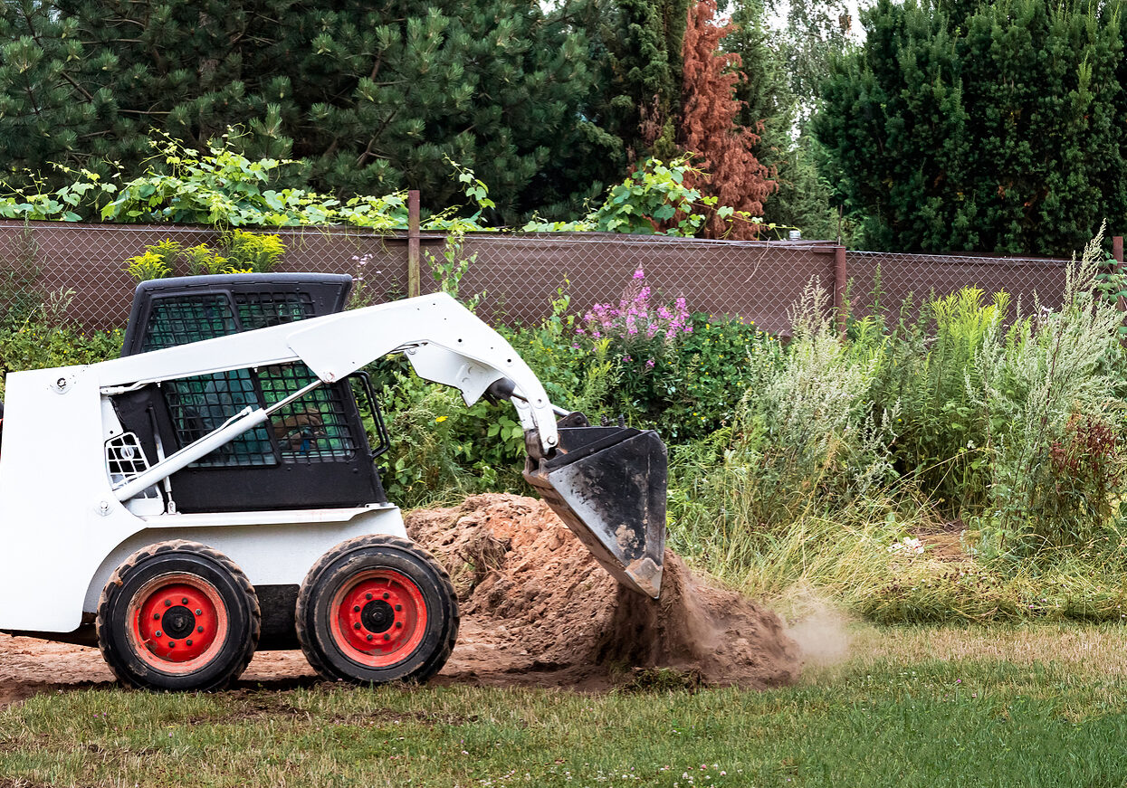 A skid steer loader clears the site for construction. Land work by the territory improvement. Machine for work in confined areas. Small tractor with a bucket for moving soil, turf and bulk materials.